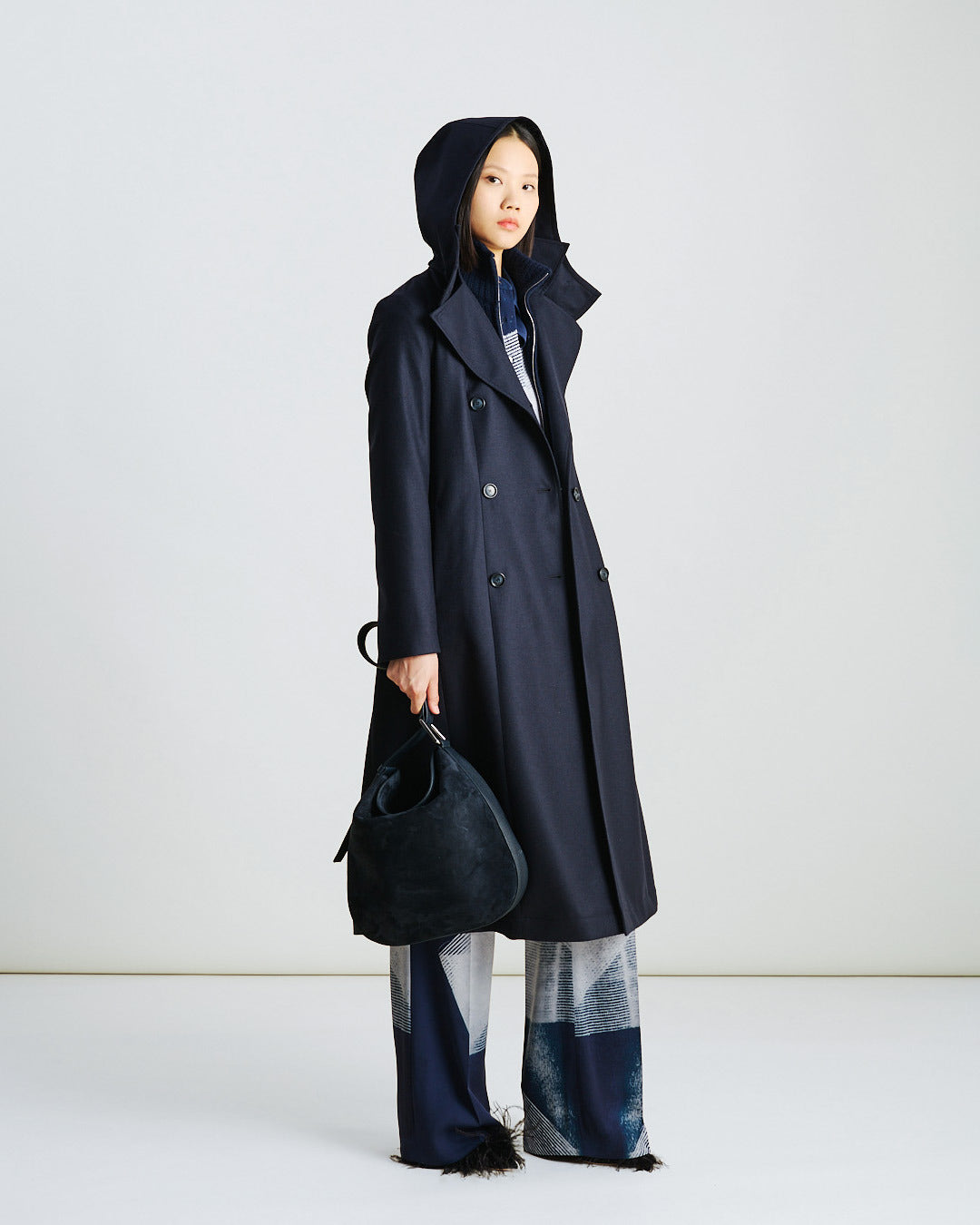 Akris Fall/Winter look featuring a printed silk ensemble — wide straight pants and a matching crepe blouse in denim ecru zigzag motif, styled under a hooded navy coat for an elegant, artistic edge.