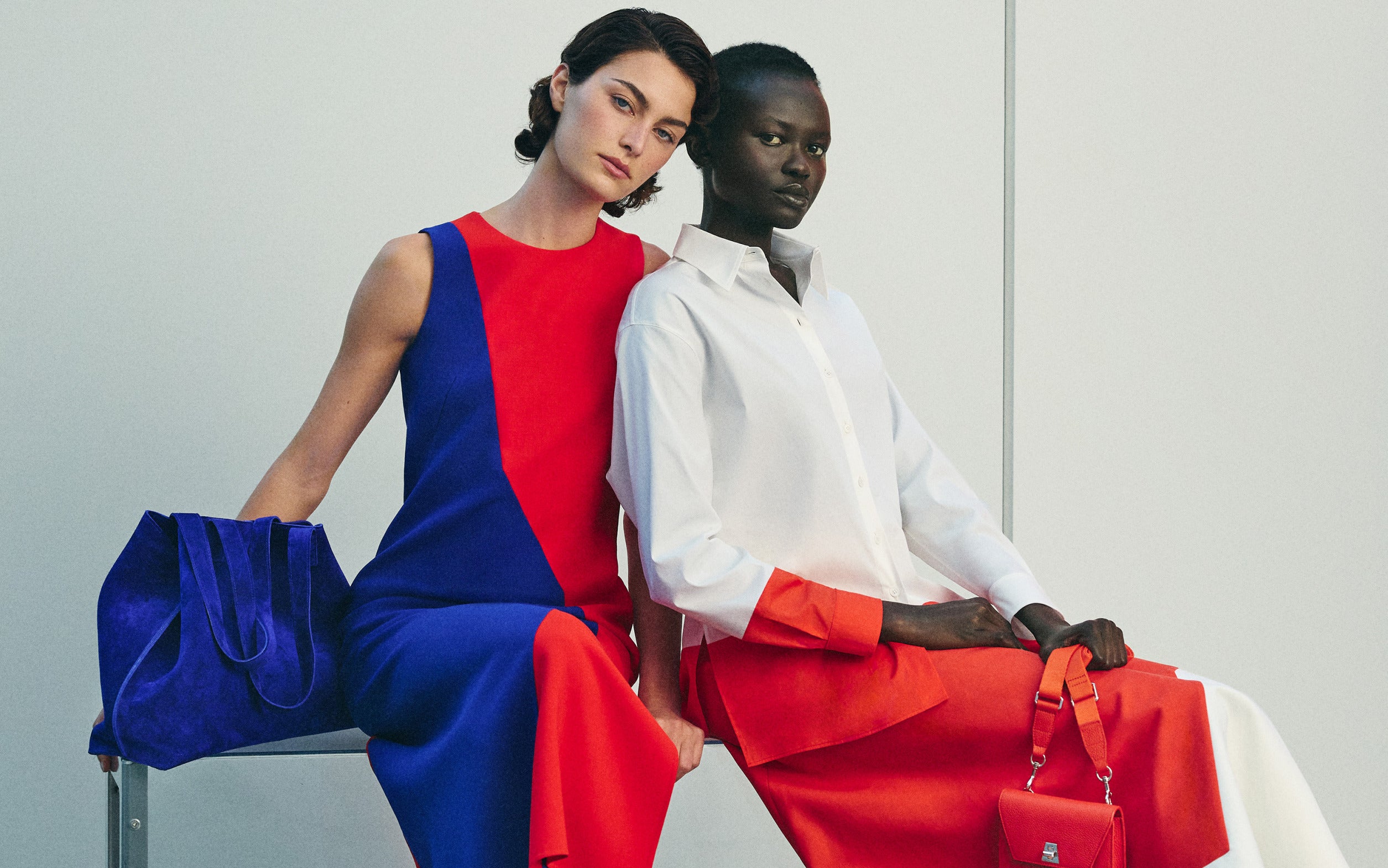 Detaillierter Produktshot eines ärmellosen, rot-blauen Etuikleids mit geometrischem Muster, kombiniert mit einer blauen Wildleder-Shopper-Tasche. Ein passendes, weißes Button-down-Baumwollhemd mit orangefarbenen Akzenten ist ebenfalls zu sehen.