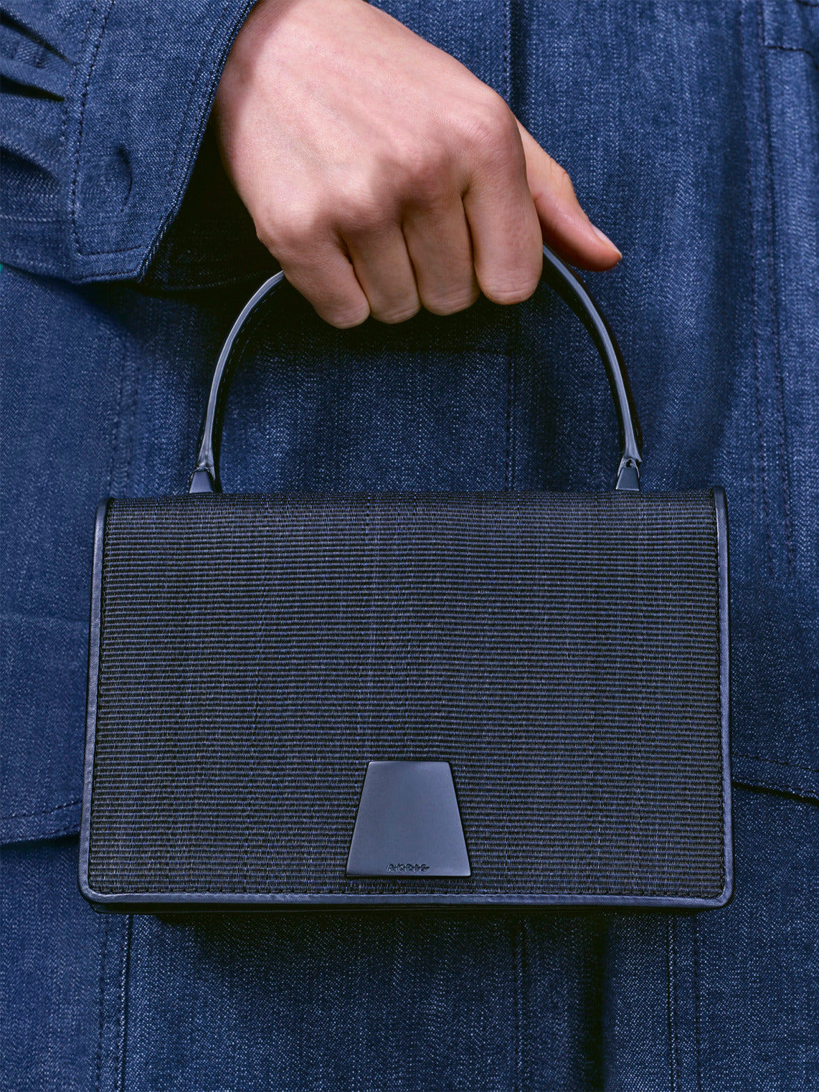 Nahaufnahme zweier strukturierter Handtaschen mit trapezförmigem Verschluss, eine in leuchtendem Rot und die andere in Schwarz.
Die Taschen werden vor passender roter Kleidung und dunklem Denim präsentiert.