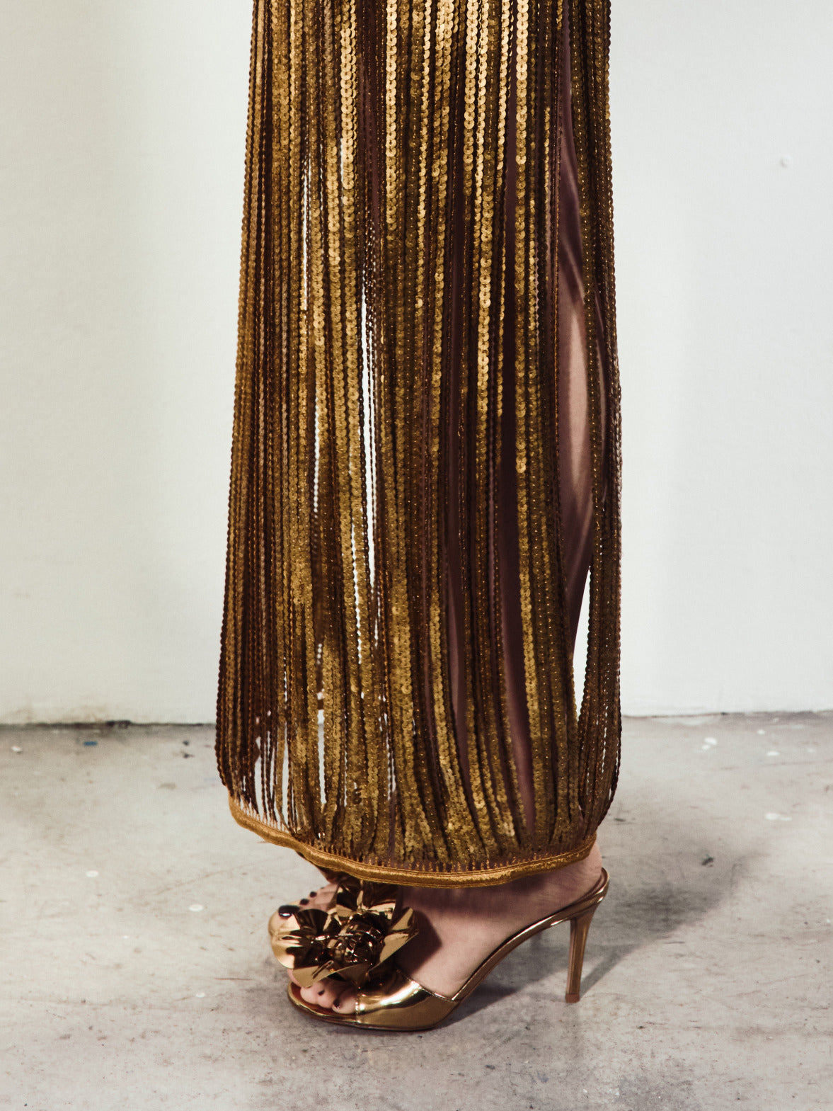A detailed shot focuses on a gold sequined fringe skirt paired with metallic stiletto sandals featuring a large decorative bow.