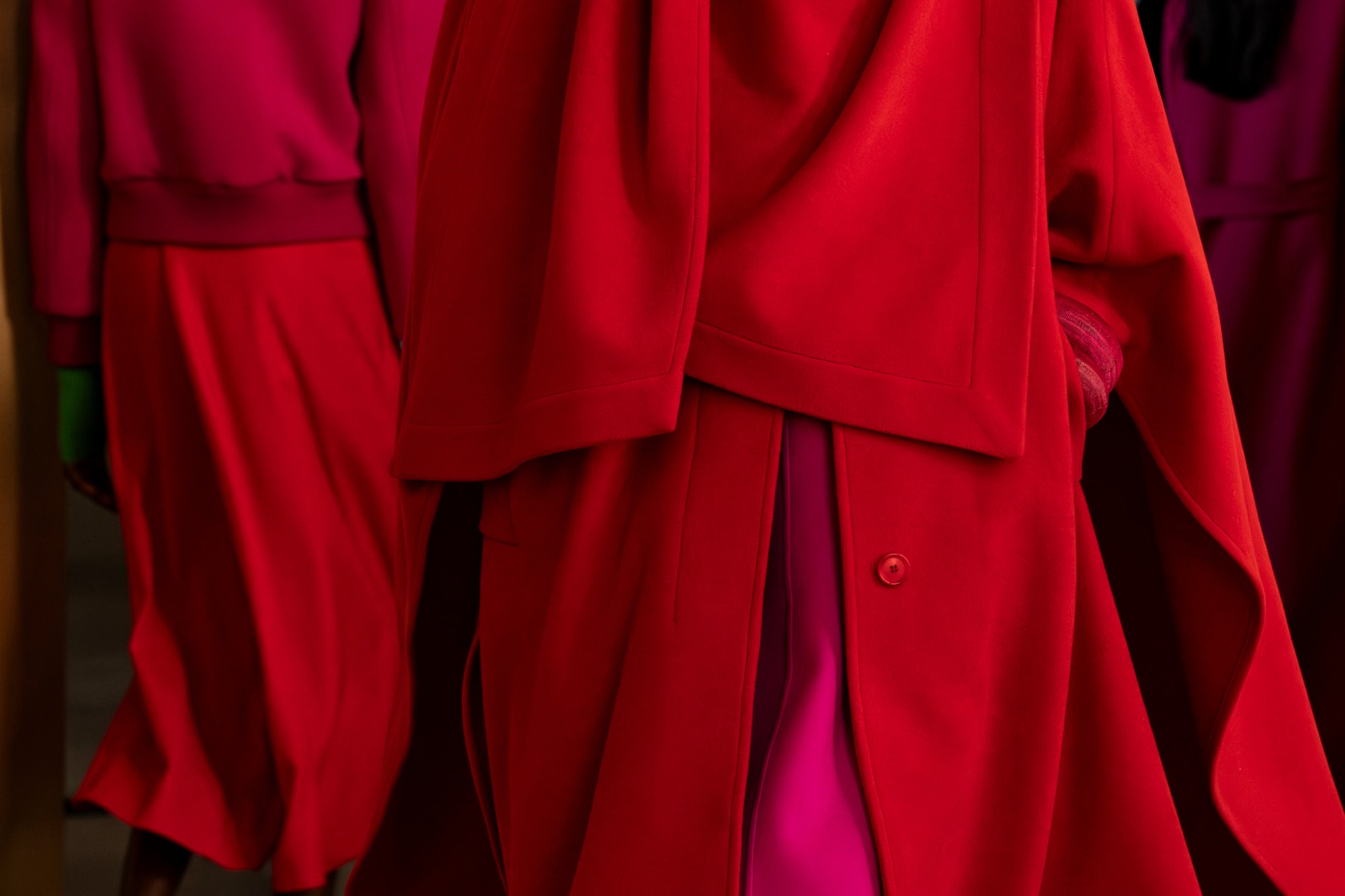 Eine lebendige Nahaufnahme von Wollgewändern in kräftigen Rot- und Magentatönen, die klare Schnitte und satte monochrome Texturen zeigen.