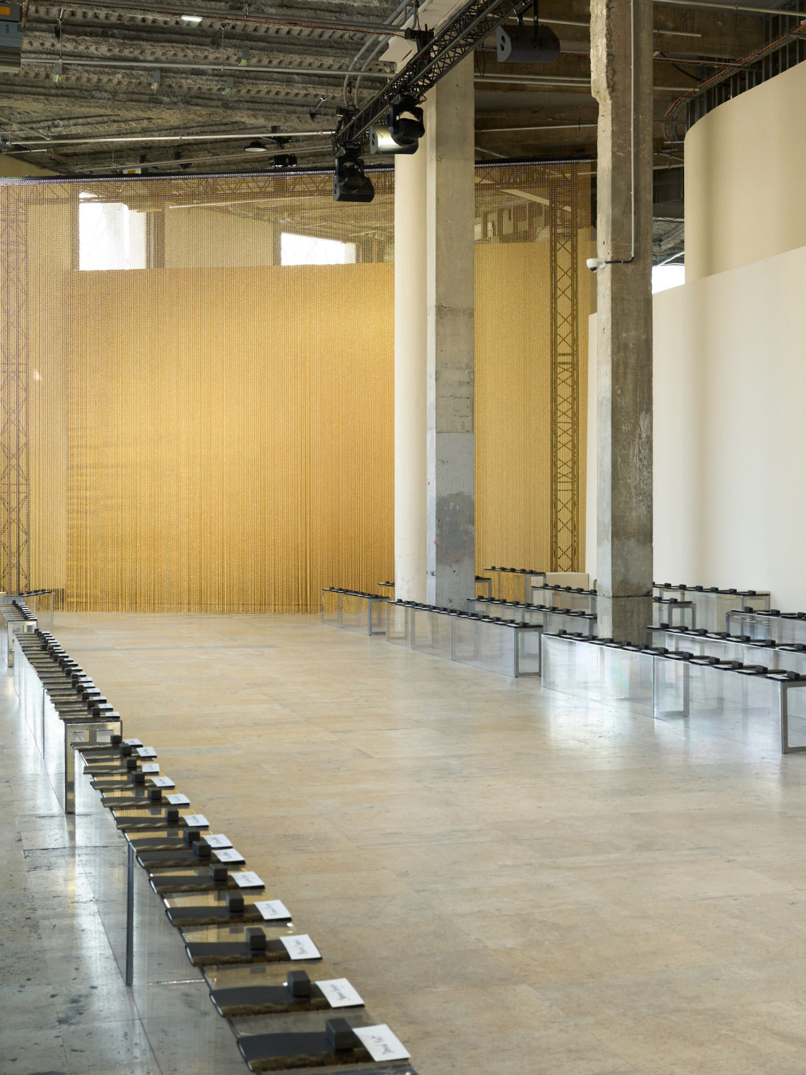 Eine Nahaufnahme eines leuchtend goldenen Perlenvorhangs, der eine dichte Wand aus schimmernden vertikalen Linien bildet, die das Licht einfangen.