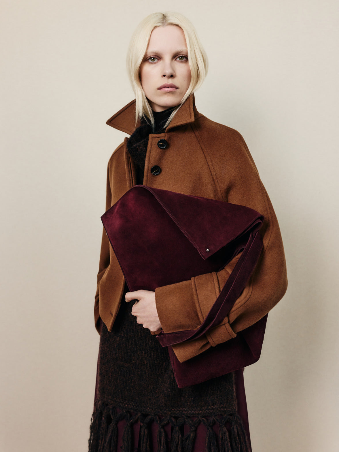 Look aus der Akris Fall 2026 Kollektion mit einer Mantelsilhouette in Camel und einer Oversize-Wildledertasche in satten Burgundytönen.