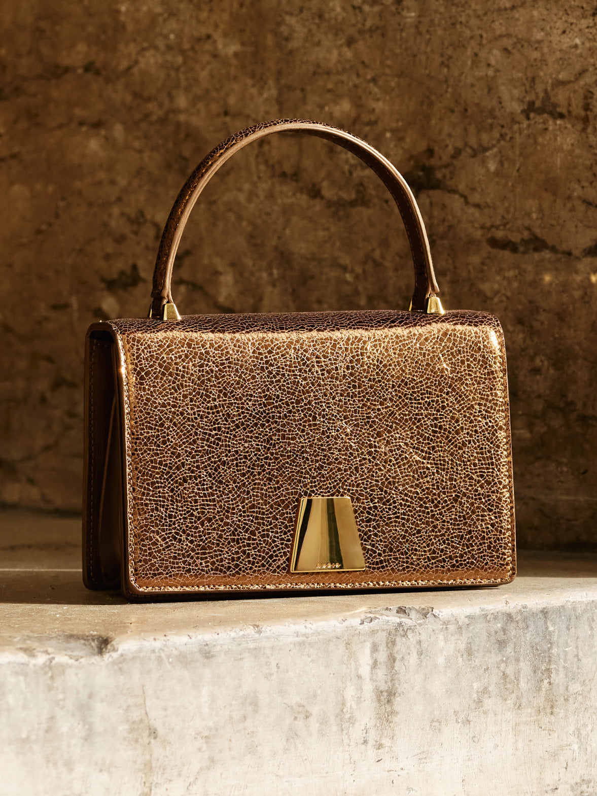 Akris Alice Top Handle Bag aus Leder in Metallic-Bronze mit strukturierter Silhouette und charakteristischem Trapezverschluss.
