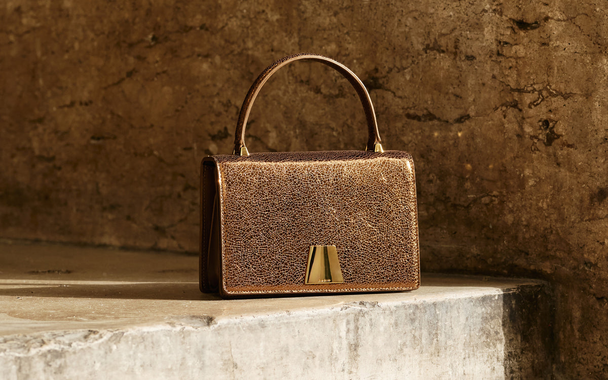 Akris Alice Top Handle Bag aus Leder in Metallic-Bronze mit strukturierter Silhouette und charakteristischem Trapezverschluss.