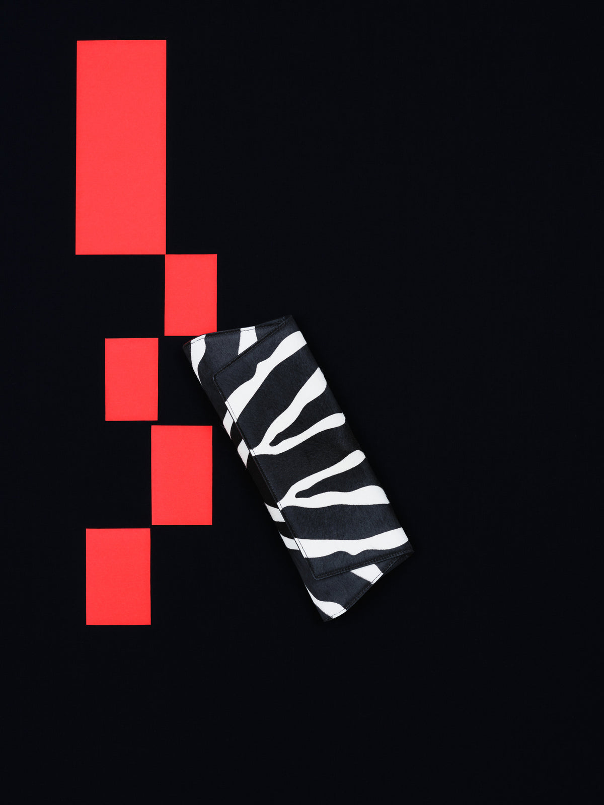 Erleben Sie die grafische Anziehungskraft der Akris Pre-Fall Kollektion mit della eleganten Anouk Clutch im markanten Zebra-Look. Vor einem minimalistischen, schwarzen Hintergrund mit leuchtend roten, geometrischen Akzenten setzt dieses Luxus-Accessoire ein stilvolles Statement. Entdecken Sie modernes Design und erstklassige Schweizer Handwerkskunst.