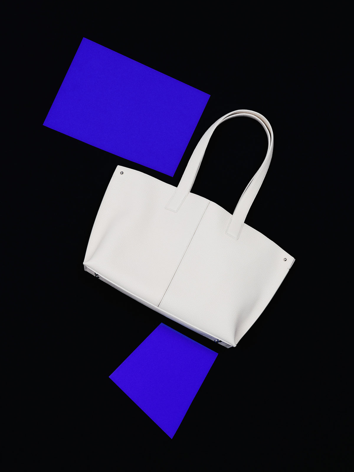 Erleben Sie den minimalistischen Perfektionismus der Akris Pre-Fall Kollektion mit der ikonischen Ai Handtasche in elegantem Weiß. Kunstvoll inszeniert vor einem tiefschwarzen Hintergrund mit leuchtend elektrisch-blauen, geometrischen Akzenten, verkörpert dieses Luxus-Accessoire pure moderne Eleganz. Entdecken Sie zeitlose Schweizer Klasse.