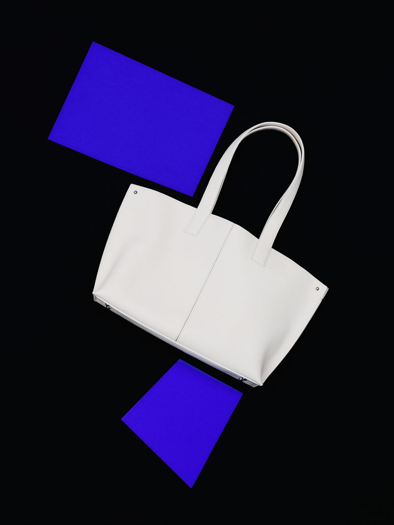 Erleben Sie den minimalistischen Perfektionismus der Akris Pre-Fall Kollektion mit der ikonischen Ai Handtasche in elegantem Weiß. Kunstvoll inszeniert vor einem tiefschwarzen Hintergrund mit leuchtend elektrisch-blauen, geometrischen Akzenten, verkörpert dieses Luxus-Accessoire pure moderne Eleganz. Entdecken Sie zeitlose Schweizer Klasse.