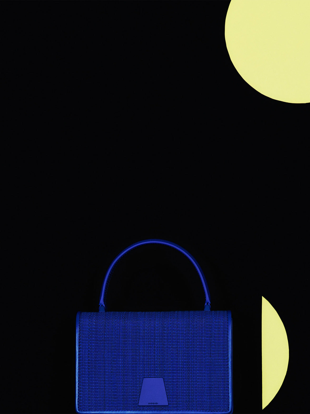 Akris Alice Handtasche aus blauem Horsehair mit strukturiertem Henkel vor schwarzem Hintergrund.
