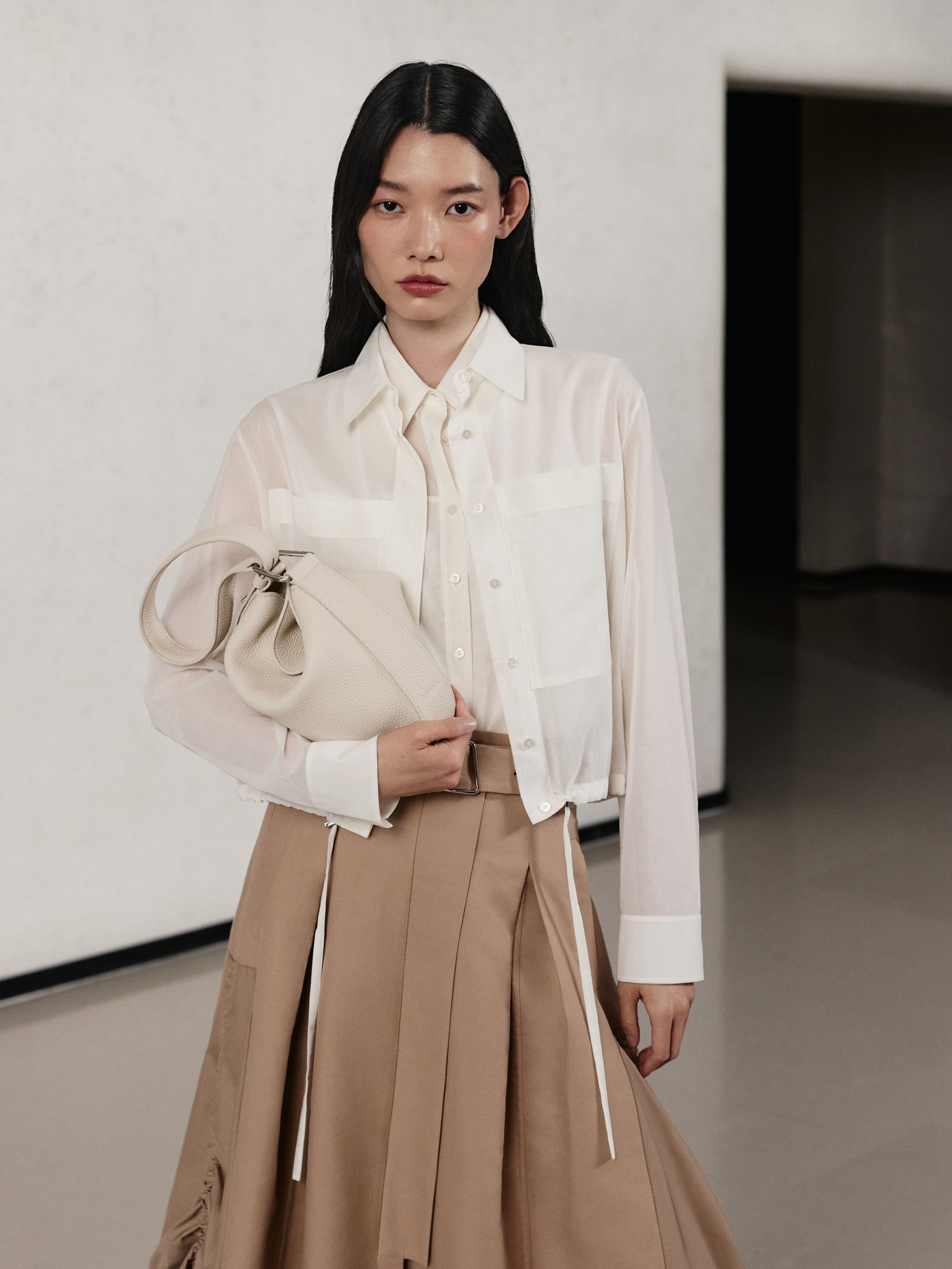 Erleben Sie mühelose Eleganz mit der Akris Pre-Fall Kollektion, bestehend aus einer klassischen weißen Bluse und einem eleganten plissierten Rock in Beige. Ergänzt wird das stilvolle Ensemble durch die weiche Anna Hobo Handtasche aus fein strukturiertem, cremeweißem Leder. Entdecken Sie minimalistischen Luxus und erstklassige Schweizer Handwerkskunst.