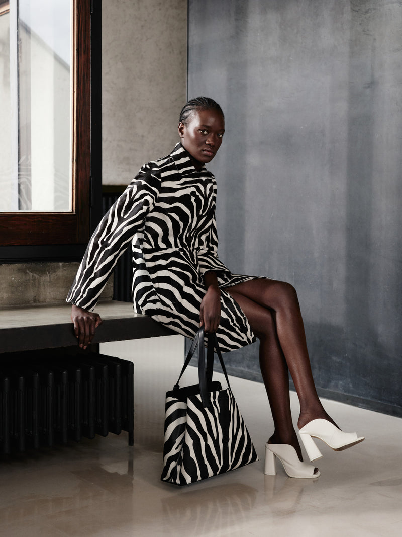 Erleben Sie ausdrucksstarke Kontraste mit der Akris Pre-Fall Kollektion und einem ikonischen Mantel im Allover-Zebra-Print. Ergänzen Sie den Look mit der passenden Ai Handtasche und eleganten, weißen Leder-Mules für ein modernes Finish. Entdecken Sie Luxusmode, die mutige Muster mit zeitloser Schweizer Handwerkskunst verbindet.
