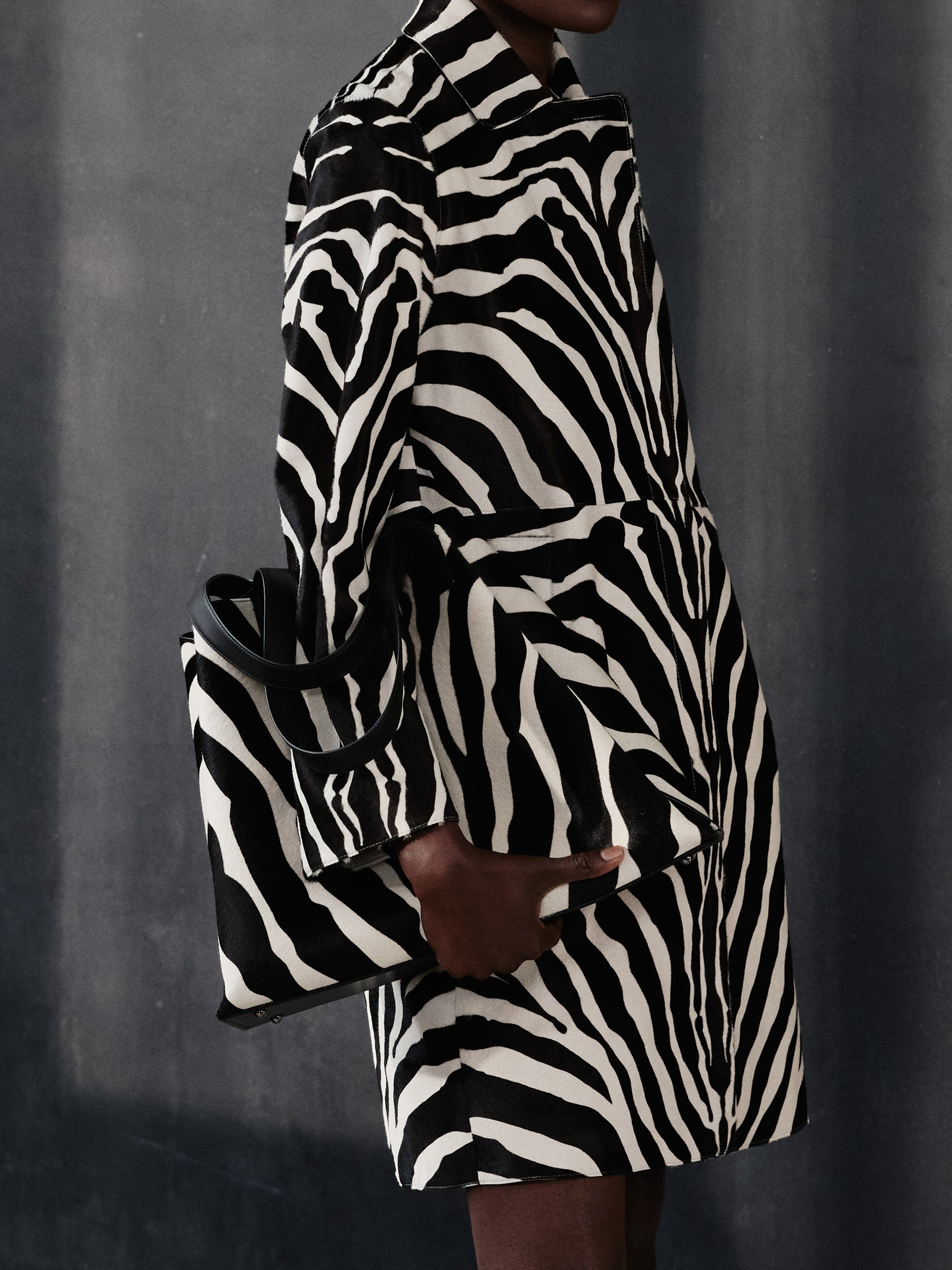Setzen Sie ein klares Statement mit dem Allover-Zebra-Print der aktuellen Akris Pre-Fall Kollektion. Kombinieren Sie den ausdrucksstarken Mantel mit der passenden, ikonischen Ai Handtasche für einen luxuriösen Monochrom-Look. Erleben Sie die perfekte Symbiose aus mutigem Design und zeitloser Schweizer Eleganz.