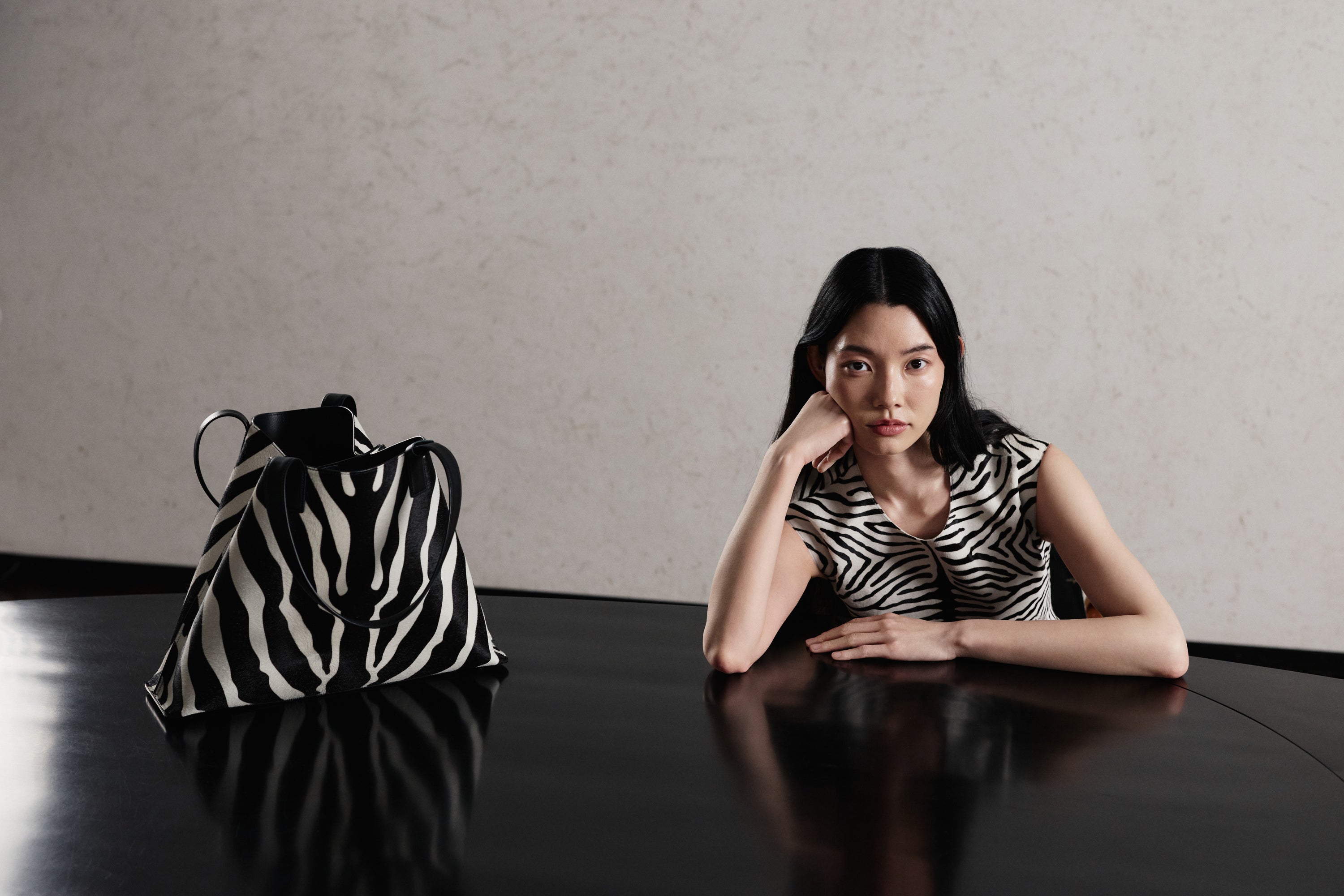 Erleben Sie die grafische Raffinesse der Akris Pre-Fall Kollektion mit einem eleganten, ärmellosen Oberteil im ausdrucksstarken Zebra-Print. Perfekt darauf abgestimmt präsentiert sich die ikonische Ai Handtasche im passenden Zebra-Look auf dem Tisch. Entdecken Sie minimalistische Silhouetten und erstklassige Schweizer Handwerkskunst.