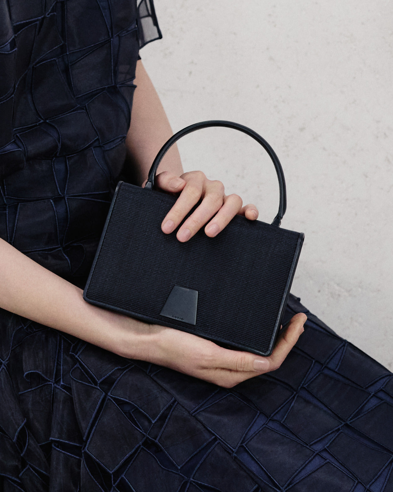Luxuriöse schwarze strukturierte Handtasche aus der Akris Pre-Fall 2026 Kollektion.
Elegante, strukturierte Designer-Tasche mit schlankem Henkel und markantem Verschluss.
Kombiniert mit einem dunkelblauen Kleid mit geometrischem Muster.