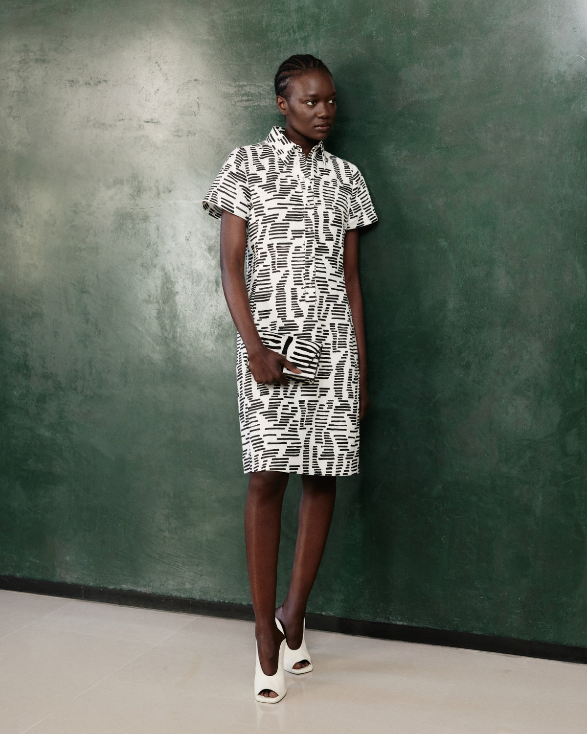 Hemdblusenkleid und passende Clutch aus der Akris Pre-Fall 2026 Kollektion.
Modernes Designer-Kleid mit abstraktem schwarz-weißem Grafikmuster.
Kurzärmeliges, knielanges Kleid kombiniert mit eleganten Open-Toe-Mules.