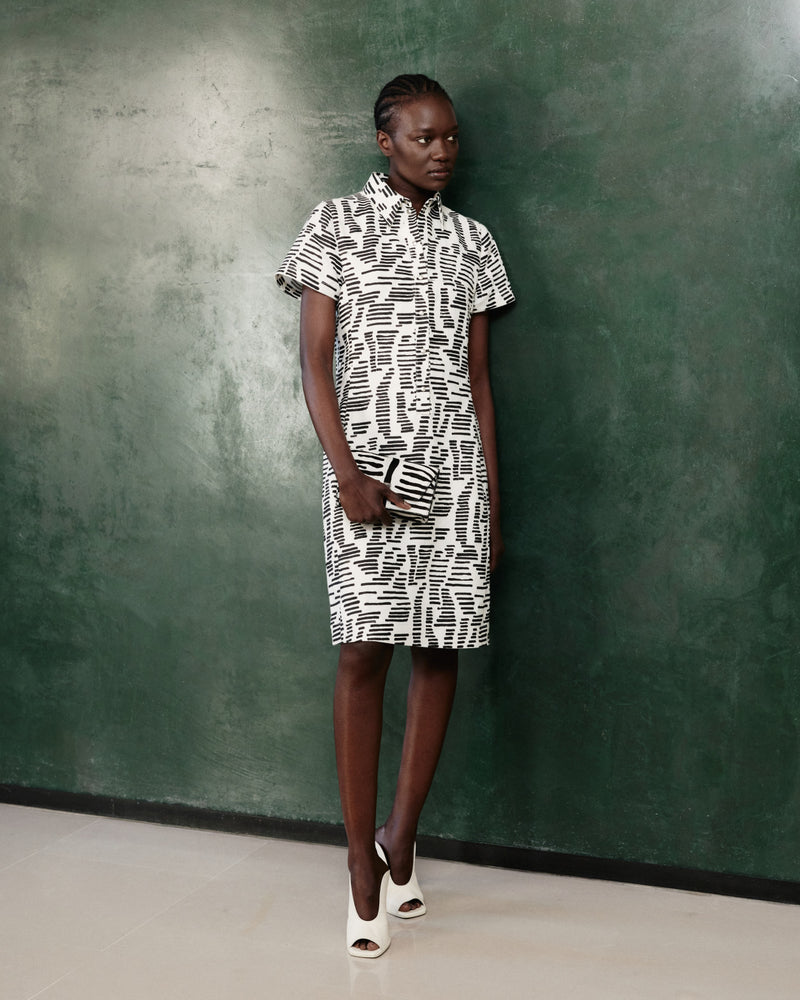 Hemdblusenkleid und passende Clutch aus der Akris Pre-Fall 2026 Kollektion.
Modernes Designer-Kleid mit abstraktem schwarz-weißem Grafikmuster.
Kurzärmeliges, knielanges Kleid kombiniert mit eleganten Open-Toe-Mules.