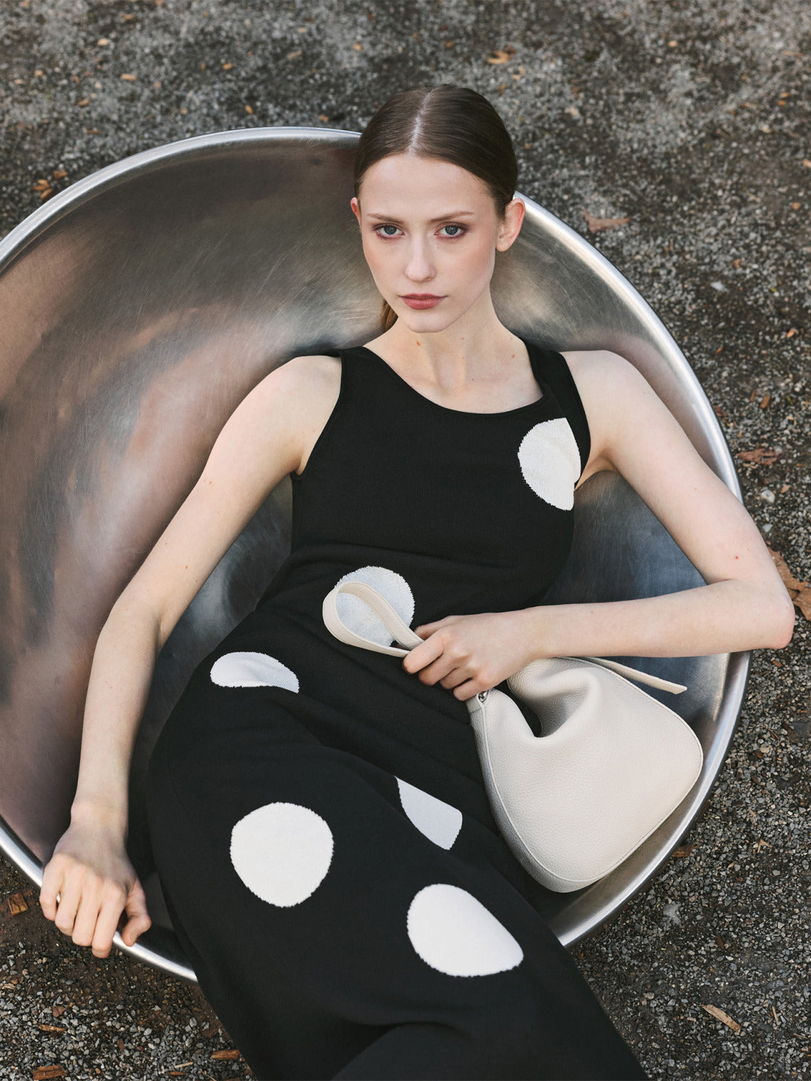 Model in einem schwarzen, ärmellosen Akris Pre-Fall 2026 Strickkleid mit Punkten, hält eine elfenbeinfarbene Ledertasche.