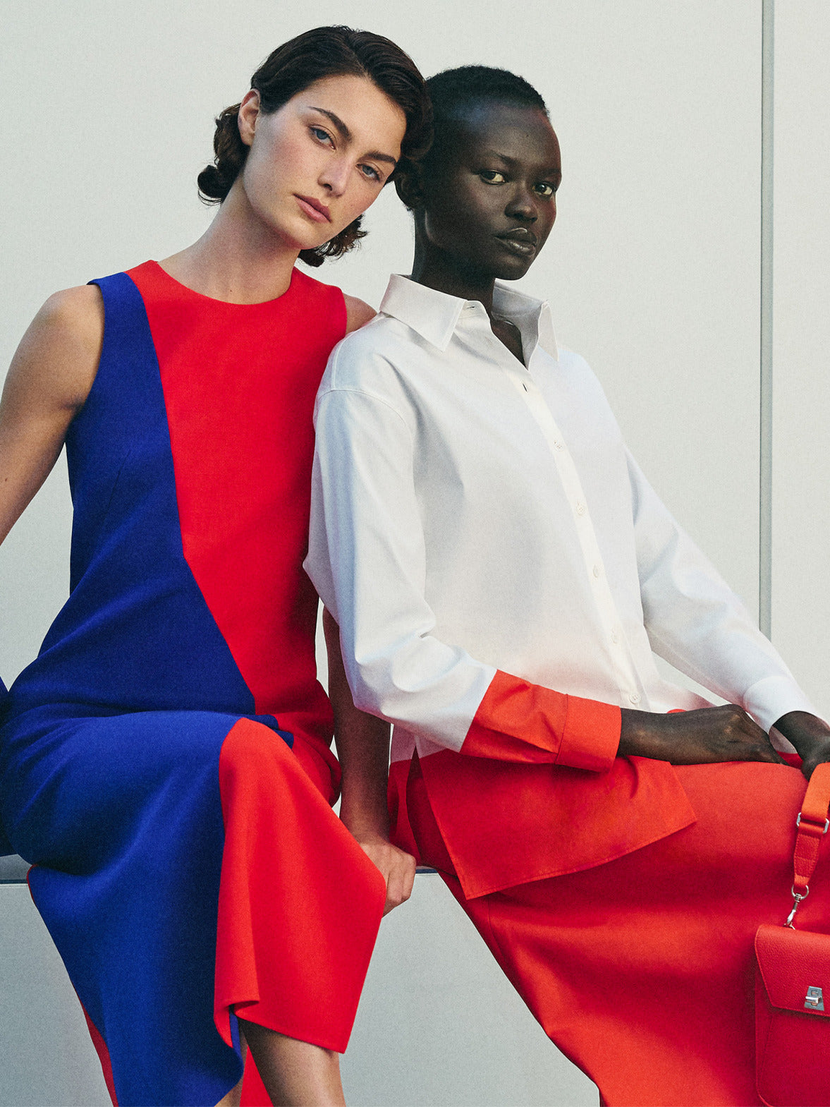 Detaillierter Produktshot eines ärmellosen, rot-blauen Etuikleids mit geometrischem Muster, kombiniert mit einer blauen Wildleder-Shopper-Tasche. Ein passendes, weißes Button-down-Baumwollhemd mit orangefarbenen Akzenten ist ebenfalls zu sehen.