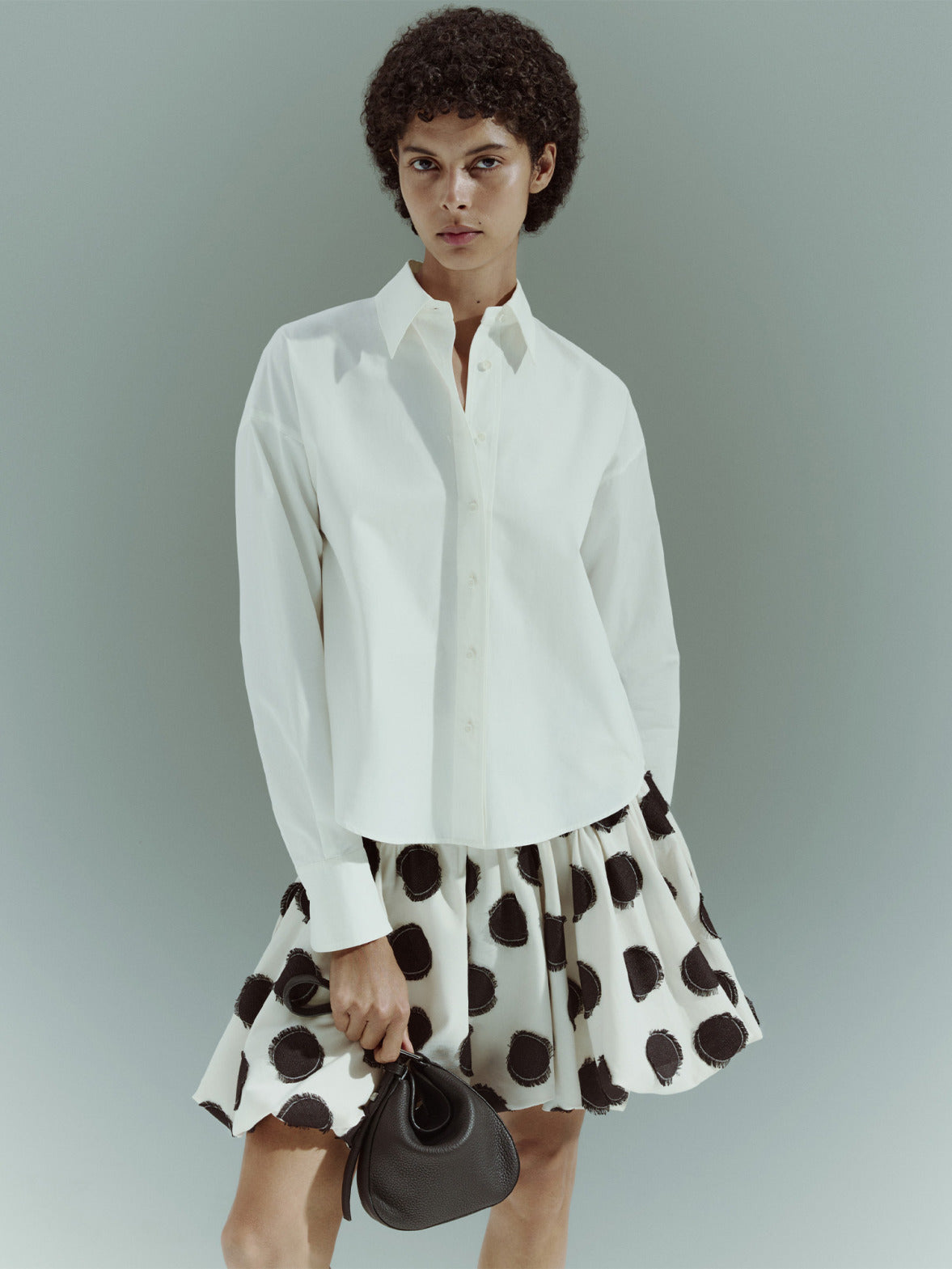 Damenmode aus der Akris punto Pre-Fall 2026 Kollektion.
Ärmelloses weißes Midikleid mit großen schwarzen Punkten.
Präsentiert neben einer klassischen langärmeligen weißen Baumwollbluse.