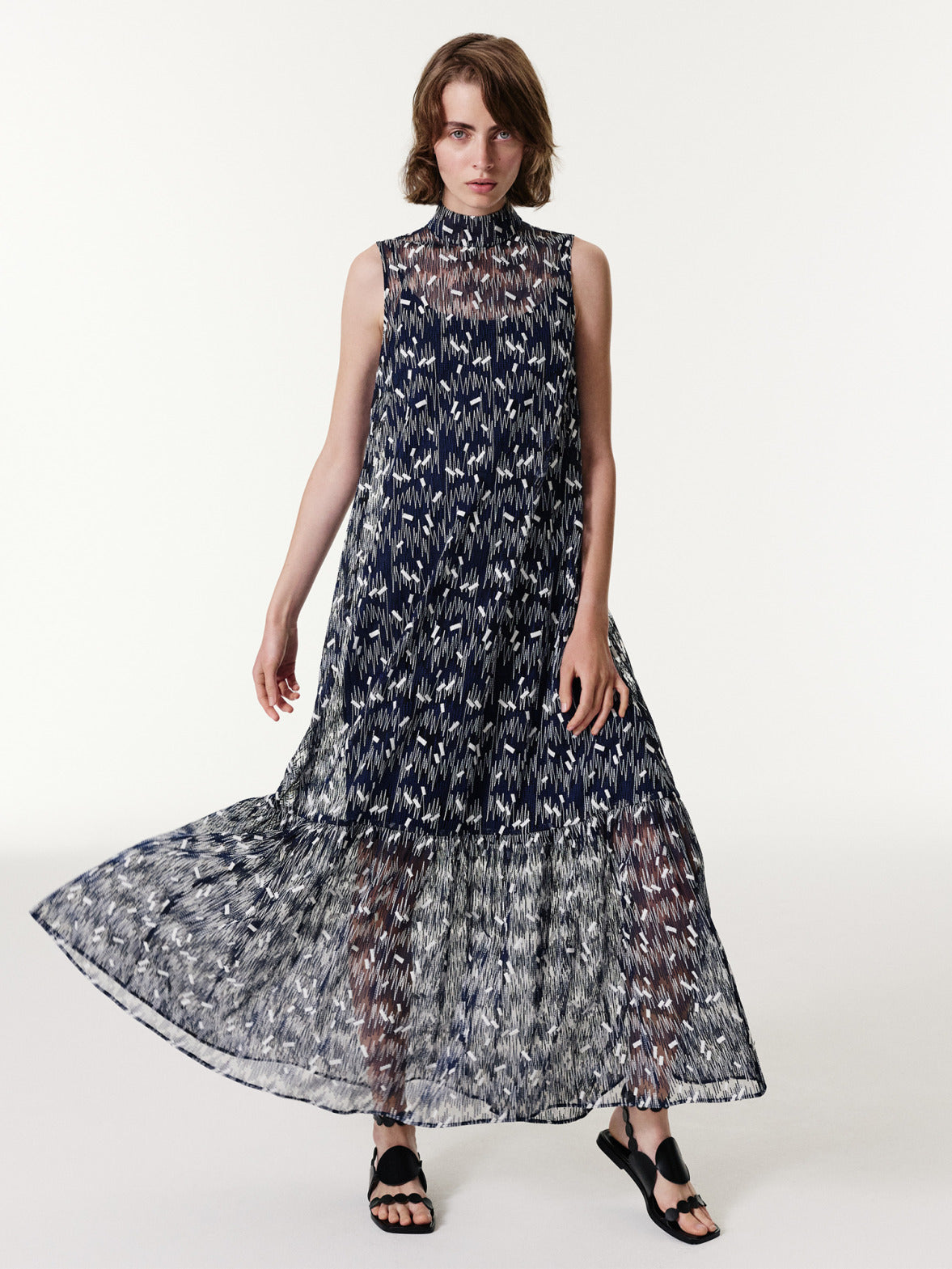 Ärmelloses Midikleid von Akris punto aus der Frühjahr 2026 Kollektion mit Stehkragen, aufwendiger geometrischer Stickerei und einem gestuften, plissierten Rock aus dunkelblauem technischem Tüll.