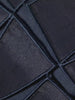Model in einem dunkelblauen, transparenten Kleid mit Gittermuster aus der Akris Pre-Fall 2026 Kollektion, sitzend auf einer minimalistischen weißen Kommode. Moderne Luxus-Damenmode mit architektonischem Design und geometrischen Texturen.